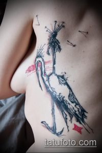Фото тату на груди: стилизованный черный журавль с красными акцентами. Рисунок татуировки в графическом стиле.