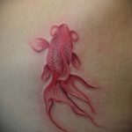 Фото акварельной татуировки золотой рыбки на плече. Мягкие переходы цветов, легкий и воздушный рисунок татуировки.