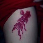 Фото тату золотой рыбки на лодыжке, выполненное в нежных розовых тонах. Эскиз татуировки с плавными линиями и акварельным эффектом.