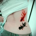 Фото тату двух золотых рыбок, одна красная, другая черная, на боку девушки, выполненных в минималистичном стиле.