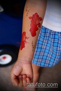 Фото простой татуировки с двумя красными рыбками на руке ребенка. Минималистичный рисунок, яркий цвет, подходит для временного нанесения.