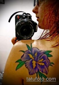 Фото тату с изображением ириса и фотоаппарата на плече. Композиция символизирует любовь к искусству, красоте и творчеству.