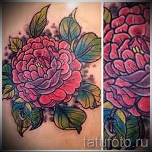Фотография татуировки с изображением пышного пиона в красных и розовых тонах, выполненной в реалистичном стиле.