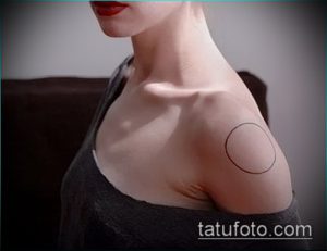 Фото минималистичной татуировки на ключице, изображающей тонкий красный круг, подчеркивающий изящные линии тела.