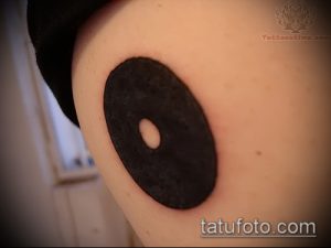 Фото тату: черная круглая татуировка с отверстием в центре, расположенная на бедре. Минималистичный и загадочный рисунок.