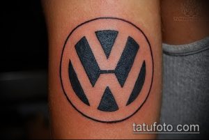 Фото тату с изображением логотипа Volkswagen на предплечье. Черный рисунок татуировки в круглой рамке, выполненный четкими линиями.