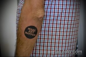 Фото тату надписи 'MAKE ART HAPPEN' в черном круге на предплечье. Простой и мотивирующий рисунок татуировки.