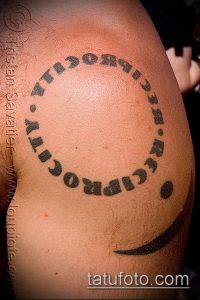 Фото тату: круговая татуировка с надписью на латыни на руке. Оригинальный и загадочный рисунок татуировки для ценителей мистики и древних языков.