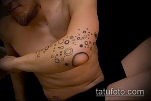 Фото тату, состоящего из множества черных кругов разного размера, расположенных на предплечье. Рисунок выглядит абстрактно и минималистично.