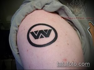 Фото тату на плече: черная буква 'W' внутри черного круга. Минималистичный рисунок татуировки, простой эскиз.