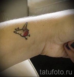 Фото тату: Милая маленькая татуировка птички с красной грудкой на женском запястье. Простой и нежный рисунок.