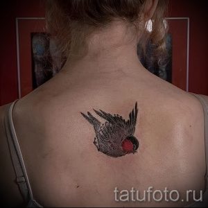 Фото тату маленькой птицы на спине. Черно-серый рисунок, минималистичный дизайн, акцент на форме и контурах.