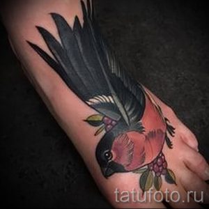 Фото тату птицы на стопе. Яркие цвета, детальная проработка перьев и веточек с ягодами. Оригинальный и стильный дизайн.