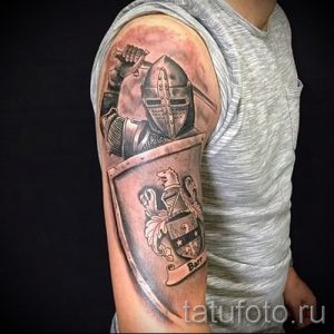 Фото тату на руке: рыцарь в доспехах с мечом и щитом, выполненный в реалистичной технике с использованием серых и черных оттенков.