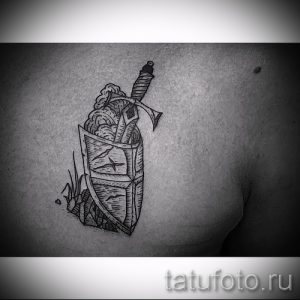 Фото тату викингского шлема и щита на груди. Черно-белый рисунок в стиле графика с четкими контурами.