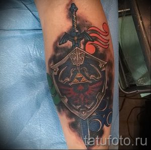 Фото тату меча и щита из игры The Legend of Zelda на предплечье. Яркий рисунок с использованием синих, красных и серых цветов.