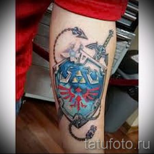 Фото цветной тату на ноге с изображением меча и щита из игры The Legend of Zelda. Яркий рисунок татуировки в стиле аниме и видеоигр.