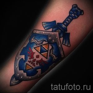 Фото тату на руке: щит и меч из популярной видеоигры The Legend of Zelda. Цветная татуировка с четкими контурами и яркими цветами.