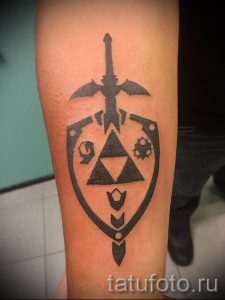Фото татуировки на руке с изображением щита и меча из игры Zelda. Простой и лаконичный рисунок татуировки в черно-белых тонах.