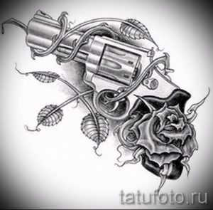 Фото тату в черно-серых тонах, изображающее пистолет, обвитый ветвями с листьями и бутоном розы. Рисунок выполнен с высокой детализацией.