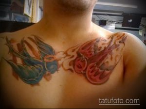 Фото тату на груди и ключицах: две ласточки, одна синяя, другая красная, выполненные в акварельном стиле.