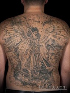 Фото масштабной татуировки архангела Михаила, сражающегося с демоном на спине. Изображение выполнено в черно-серых тонах с детализированными облаками и фигурами.