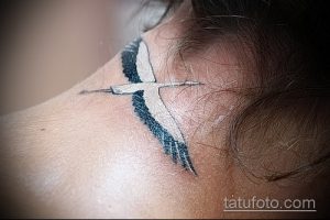 Фото небольшой татуировки аиста за ухом. Черно-белый рисунок с акцентом на изящные линии и силуэт птицы.