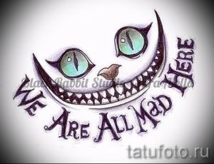 Фото тату Чеширского кота с безумной улыбкой и надписью 'We Are All Mad Here'. Рисунок выполнен в ярких цветах, идеально подходит для поклонников 'Алисы в Стране чудес'.