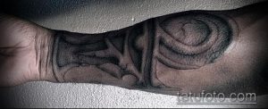 Черно-белое фото татуировки Анкх на запястье, выполненной в технике Blackwork. Крупный, графичный рисунок с использованием плотных черных заливок.