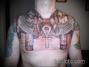 Фото красочной татуировки на груди и плечах, выполненной в древнеегипетском стиле. Изображены боги, Анкх, крылья и колонны.