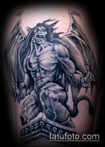 Фото тату демона на руке, выполненное в черно-серых тонах. Детализированный рисунок с крыльями, рогами и кирпичной стеной, демонстрирующий мастерство тату-художника.