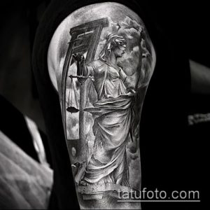 Черно-серое фото тату на руке, изображающее богиню Фемиду с весами и мечом, выполненное в реалистичном стиле с детализированной проработкой.