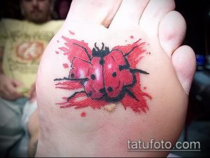 Фото тату божьей коровки в акварельной технике на стопе. Яркий и красочный рисунок татуировки с эффектом размытия.