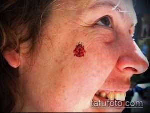 Фото тату маленькой красной божьей коровки на щеке женщины. Необычное и минималистичное расположение татуировки.