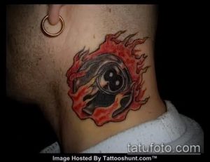 Фото татуировки бильярдного шара номер восемь, окруженного языками пламени, выполненной в ярких цветах.
