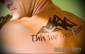 Фото тату с изображением гор и надписью "This too shall pass" на спине. Черно-белый рисунок татуировки, символизирующий надежду и веру.