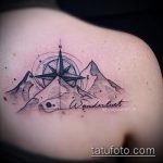 Фото тату: небольшая татуировка горного пейзажа с компасом и надписью 'Wanderlust' на плече, выполненная в черно-сером стиле.