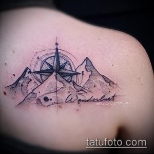 Фото тату: небольшая татуировка горного пейзажа с компасом и надписью 'Wanderlust' на плече, выполненная в черно-сером стиле.