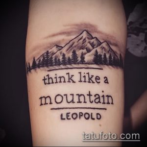 Черно-белая татуировка с изображением горного пейзажа и надписью "think like a mountain" на предплечье. Рисунок татуировки с цитатой.