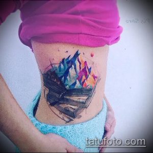 Яркая акварельная татуировка на боку с изображением горного пейзажа и падающего дома, выполненная в красочных тонах.