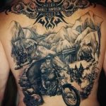 Масштабная татуировка на спине с изображением мотоциклиста на мотоцикле Harley Davidson, едущего по горной дороге. Логотип Harley Davidson и горный пейзаж.