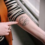 Фото тату: татуировка в форме круга с изображением горного пейзажа, выполненная в черном цвете на руке.