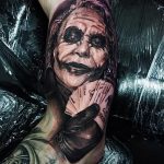 Фото тату реалистичного изображения Джокера с игральными картами на предплечье. Детализированный рисунок с использованием черных и серых оттенков.