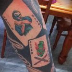 Фото татуировки на ноге с изображением двух карт Джокера. Рисунок выполнен в стиле традиционной татуировки с использованием ярких цветов.