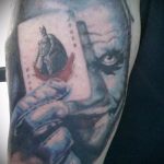 Фото татуировки с изображением Джокера, держащего карту с Бэтменом. Рисунок выполнен в стиле комикс с использованием ярких цветов и четких линий.