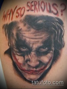 Фото тату Джокера с надписью 'Why So Serious?', выполненное в черно-серых тонах на руке.