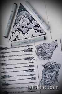 Черно-белый эскиз татуировки с изображением гор, треугольника, волка и медведя. Рядом с рисунком маркеры и другие эскизы.