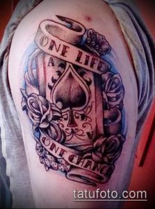 Фото тату на плече с изображением туза пик, роз и ленты с надписью 'One Life, One Chance'. Рисунок татуировки в черно-серых тонах.