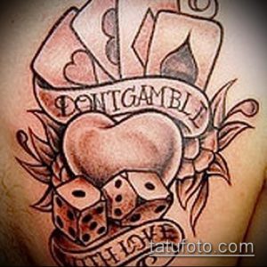 Фото тату на руке: изображение сердца, игральных костей и карт с надписью "Don't Gamble With Love", выполненное в черно-серых тонах.