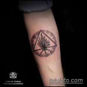 Фото тату в стиле blackwork с изображением пламени внутри треугольника. Татуировка выполнена черными чернилами и имеет геометрический дизайн.